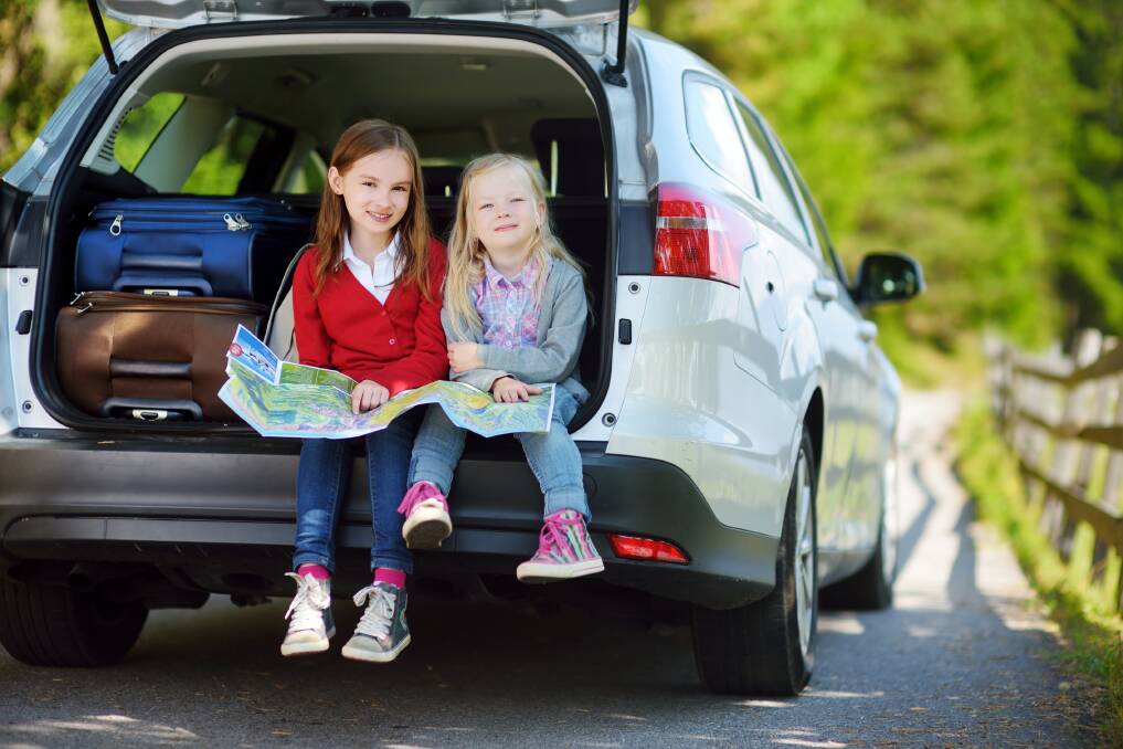 Two young girls holding a map while sitting in the back of a station wagon with suitcases. Shutterstock