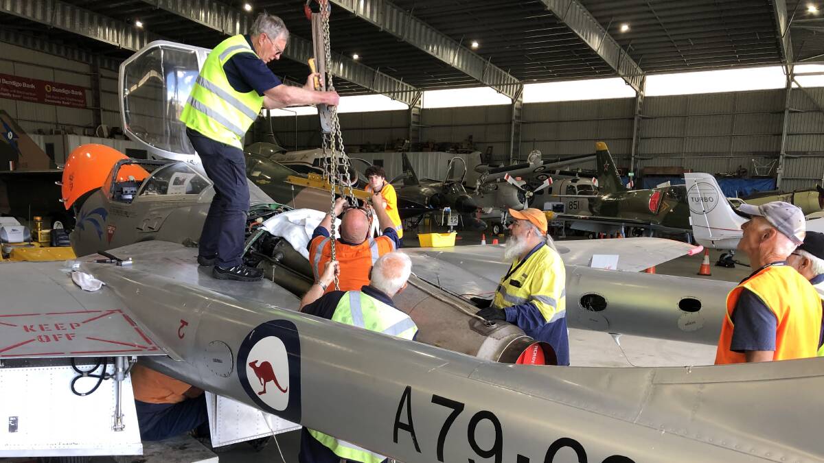 Vampire restoration team members re-install the aeroplane's engine. Picture by Ian Badham