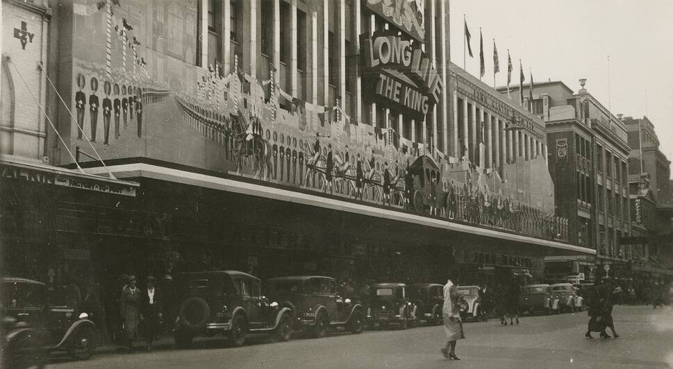 John Martin Department Store ('Johnnies') frontage in Rundle Street, Adelaide, decorated for the Coronation parade on 12 May 1937. A sign says 'Long live the King' and cutouts of a royal carriage and soldiers adorn the front of the store. Pedestrians are crossing the street in front of row of parked cars. Picture by State Library of South Australia, PRG 287/1/4/50