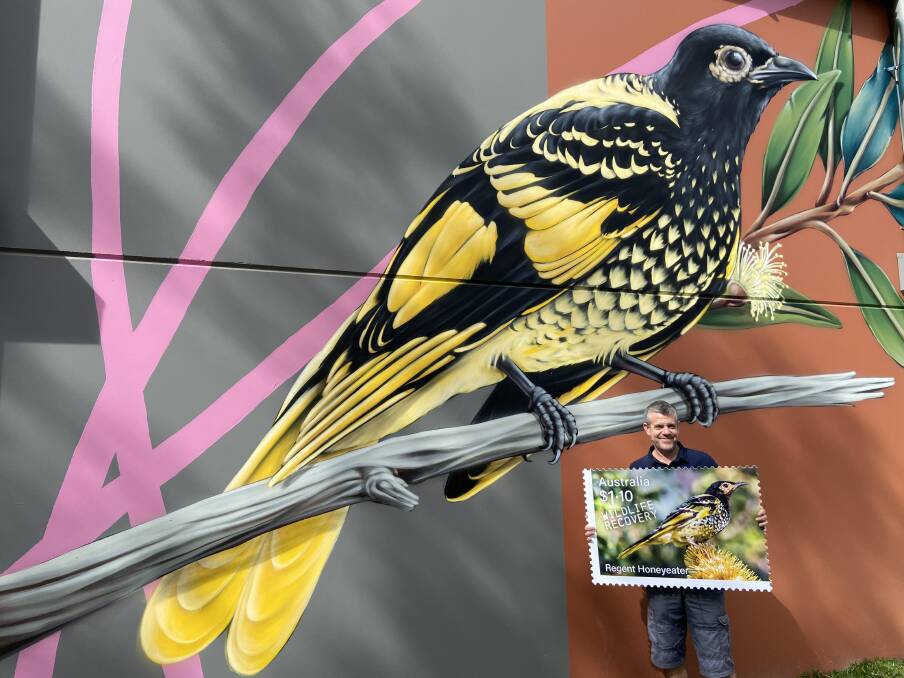 Mick Roderick stands beside the magnificent mural of a Regent Honeyeater at Pokolbin Distillery in Pokolbin, with an oversized version of the new stamp.
