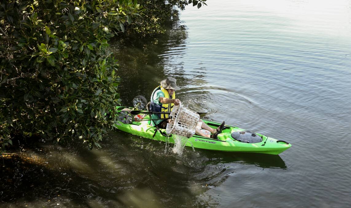 Michael Gormly fishes a plastic washing basket out of the mangroves along Throsby Creek. Picture: Marina Neil